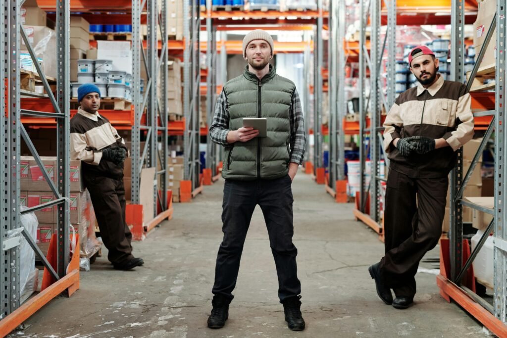 Three men in a warehouse standing among shelves with inventory.
